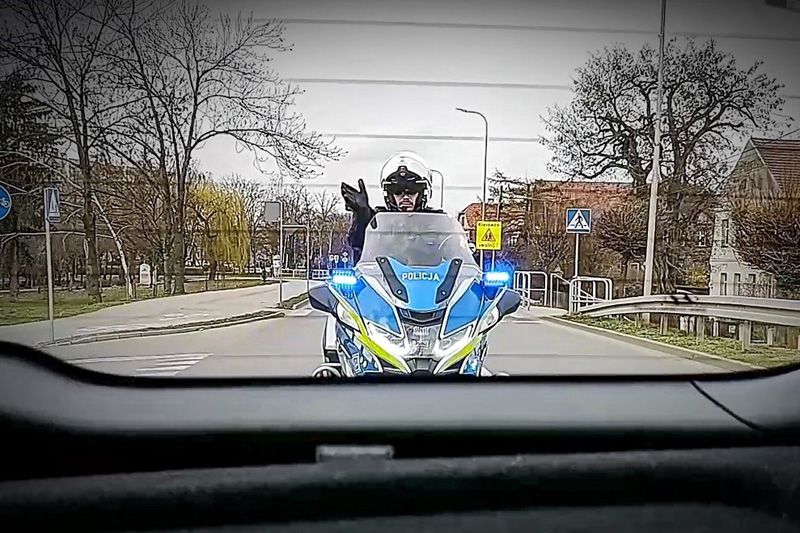 Policjant na motocyklu widoczny w tylnej szybie samochodu.