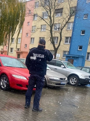 Policjant stoi na perkingu w pobliżu bloku i rozmawia z osobą na kwarantannie