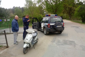 Policjant legitymuje mężczyznę. Obok policjanta stoi radiowóz, a obok mężczyzny motocykl.