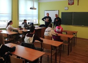 Klasa szkolna. Zawodnicy w ławkach szkolnych podczas rozmowy z policjantami.