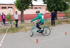 Teren przy szkole. Zawodnik pokonuje slalom na rowerze.