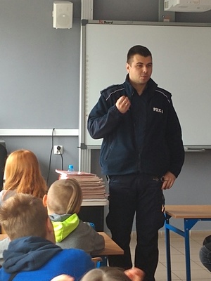 Sala lekcyjna. Policjant prowadzący zajęcia z uczniami.