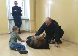 Sala szkolna. Dziecko bawiące się z psem Bossem pod bacznym okiem policjantów.