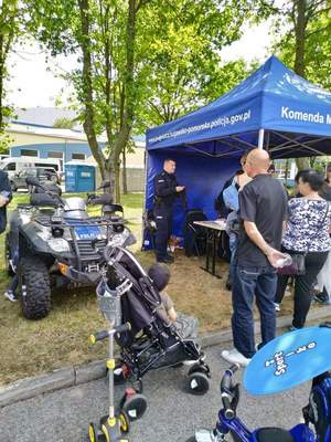 Teren wystawy &quot;AIR FAIR 2019&quot;. Stoisko policyjne (namiot), Obok stojący sprzęt policyjny, m. in. quad. Policjanci rozmawiają z dorosłymi uczestnikami wystawy.