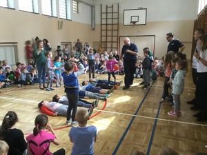 Sala gimnastyczna. Grupa dzieci uczestniczy w pogadance z policjantem. Wybrane dzieci uczestniczą w scence przechodzenia przez pasy.