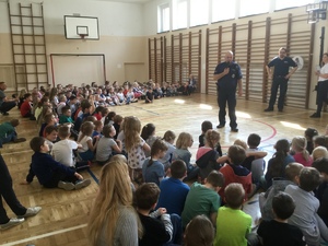 Sala gimnastyczna. Grupa dzieci uczestniczy w pogadance z policjantem.