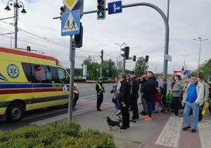 Skrzyżowanie ulic przy stadionie. Policjanci ruchu drogowego wstrzymują ruch kibiców na przejściach dla pieszych, przepuszczając karetkę pogotowia.