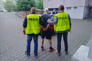 Dwaj policjanci prowadzą skutego w kajdanki mężczyznę do policyjnego pojazdu