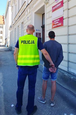 policjant prowadzi zatrzymanego skutego kajdankami