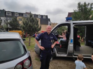 Policjant podczas festynu. Tło stanowi radiowóz, który oglądają dzieci.