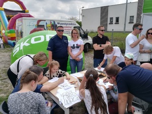 Dzieci rozwiązują krzyżówki, malują przy policyjnym stanowisku. Przygląda się temu policjant oraz pracownik policji.