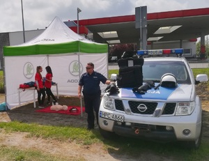 Policjant przy radiowozie, na którym również jest wyeksponowany sprzęt będący na wyposażeniu.