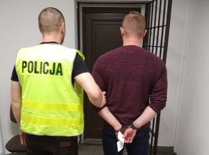 Policjant prowadzi zatrzymanego mężczyznę.