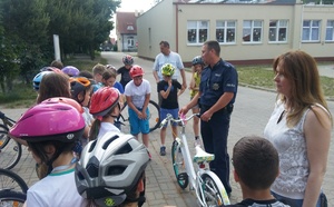 Teren zewnętrzny szkoły. Dzielnicowy mł. asp. Łukasz Libera rozmawia z dziećmi, które mają ze sobą rowery.