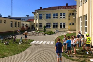 dzieci stoją i przyglądają się jak jeden z uczniów przejeżdża rowerem plac manewrowy przy szkole