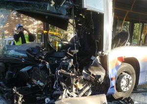 Zdjęcie jednego z rozbitych autobusów, przy którym policjant ruchu drogowego wykonuje czynności.