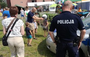 Policjanci podczas &quot;Salezjańskich Dni Młodości&quot; w Szkole Podstawowej przy ul Salezjańskiej 1 w Bydgoszczy. W tle uczestnicy festynu, w tym dzieci przymierzające elementy umundurowania bojowego.