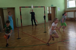 Uczniowie podczas konkurencji biegowych. W tle sędziująca policjantka.