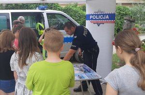 Młodzież stoi przy stoisku policyjnym w Ogrodzie Botanicznym.  W tle policjant.