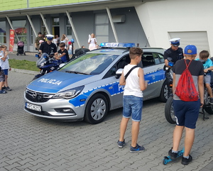 Policjanci na pikniku rodzinnym prezentują uczestnikom, głównie dzieciom, policyjny radiowóz oraz motocykl.