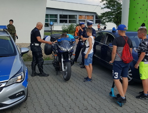 Policjanci na pikniku rodzinnym prezentują uczestnikom policyjny motocykl, na którym siedzi dziecko.