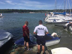 policjant stoi razem z mężczyzną na pomoście, do którego przycumowana jest łódź motorowa