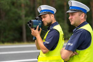 jeden z dwóch policjantów mierzy prędkość ręcznym miernikiem prędkości