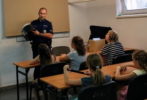 Policjant podczas pogadanki z dziećmi prezentuje wyposażenie policji wykorzystywane np. podczas imprez masowych.