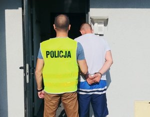 Policjant stoi z zatrzymanym przed wejściem do policyjnej izby zatrzymań.