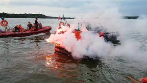 Policyjna łódź motorowa oraz ponton innych służb podpływają do osób na tratwie.