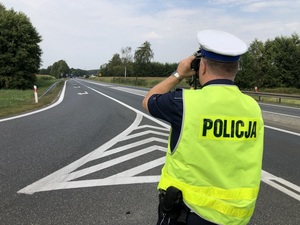 Policjant wypatruje przez lornetkę samochody na drodze