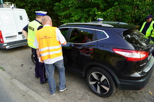 Policjant wraz z pracownikiem kolei rozmawiają z kierowcą przejeżdżającym przez przejazd.