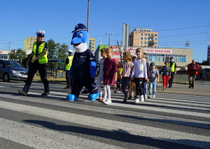 Dzieci wraz z Polfinkiem i policjantami przechodzą przez przejście dla pieszych.