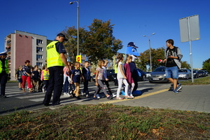 Policjant prowadzi dzieci przez przejście dla pieszych.