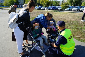 Policjant wręcza małym dzieciom w wózkach dziecięcych odblaski.