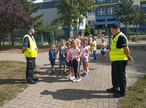 Dzieci w towarzystwie policjantów przechodzą przez przejście dla pieszych.