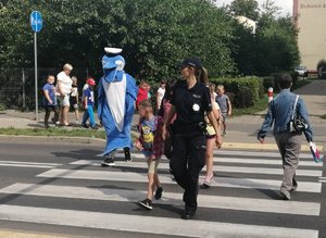 Dzieci w towarzystwie policjantki i Polfinka przechodzą przez przejście dla pieszych.