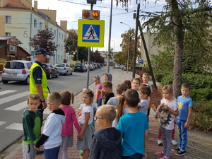 Policjant rozmawia z dziećmi przed przejściem dla pieszych.