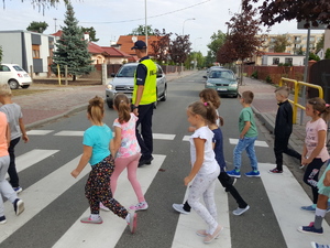 Policjant przechodzi z dziećmi przez przejście dla pieszych.