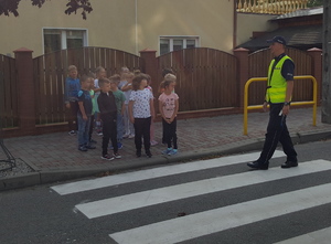 Policjant rozmawia z drugą grupą dzieci przy przejściu dla pieszych.