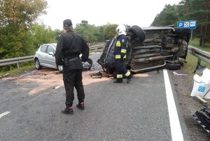 Uszkodzone pojazdy na miejscu zdarzenia. Jeden z nich leży na boku. Przy nich czynności wykonują strażacy.