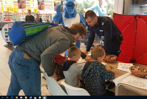 Policjanci w CH Auchan podczas akcji. Przy stoisku policyjnym dzieci rozwiązują zadania.