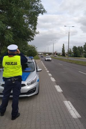 policjant obserwuje przez lornetkę kierowców, którzy korzystają z telefonu komórkowego podczas jazdy