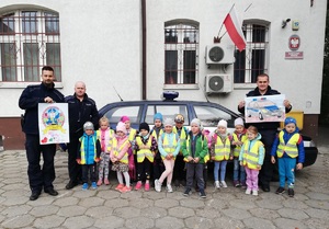 Zdjęcie grupowe policjantów z dziećmi przed budynkiem komisariatu.