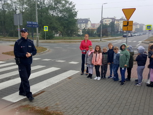 Policjant rozmawia z dziećmi przy przejściu dla pieszych.