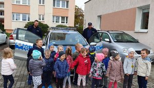 Teren przy przedszkolu. Dzieci oglądają radiowóz, przy którym stoją policjanci.