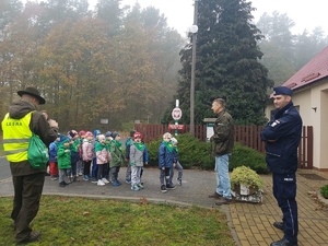 Policjant i leśnicy rozmawiają z dziećmi w lesie.