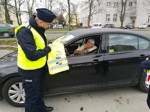 Policjant wręcza kierującej kamizelkę odblaskową dla dziecka.