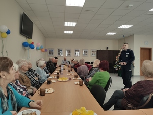 Policjant rozmawia z seniorami podczas spotkania w sali.