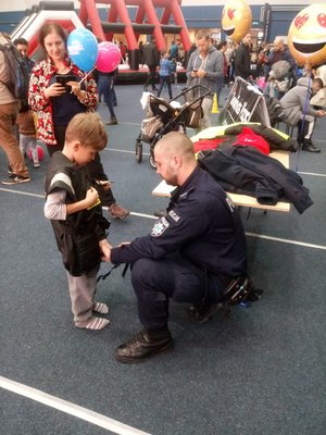 Policjant rozmawia z dzieckiem. W tle inni uczestnicy akcji &quot;Mikołajkowej&quot;.